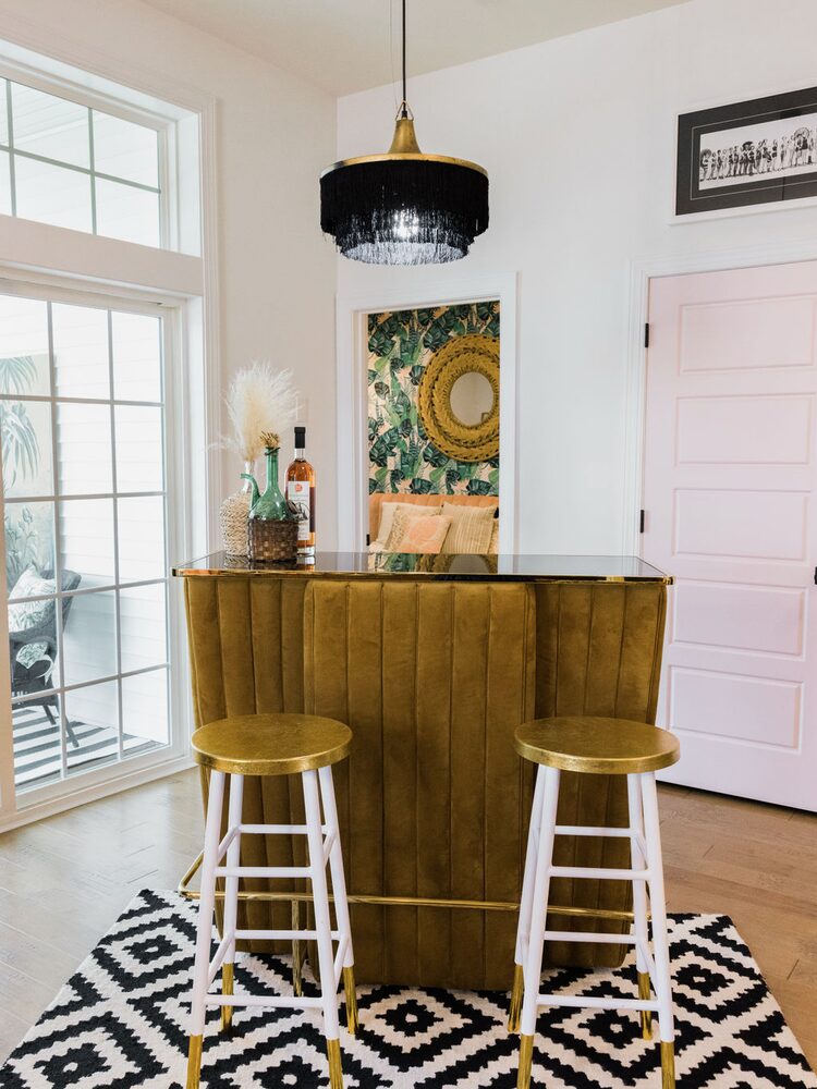 The same room styled as a home bar with velvet bar, gold stools, and botanical wallpaper